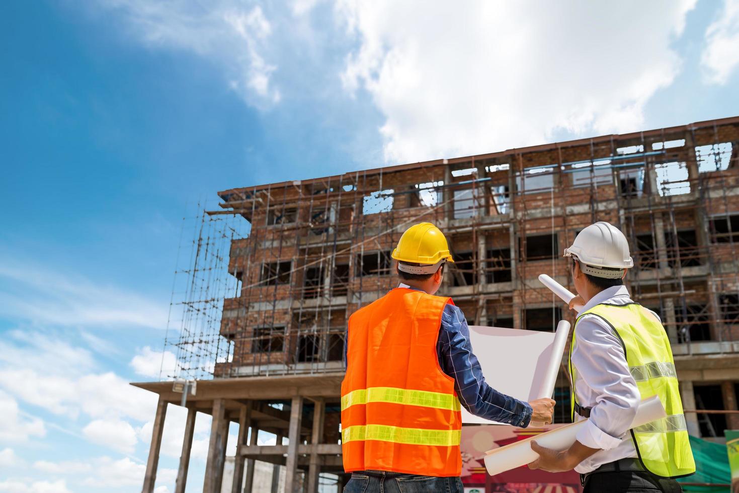 businessman and engineer looking at a building blueprint at a high rise building construction site free photo